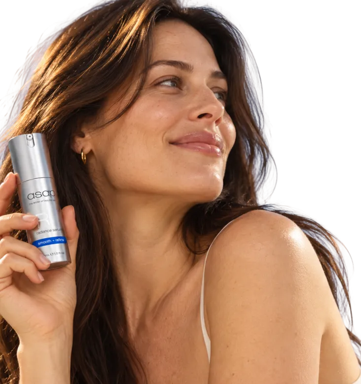 A smiling woman holding a serum dropper to her cheek
